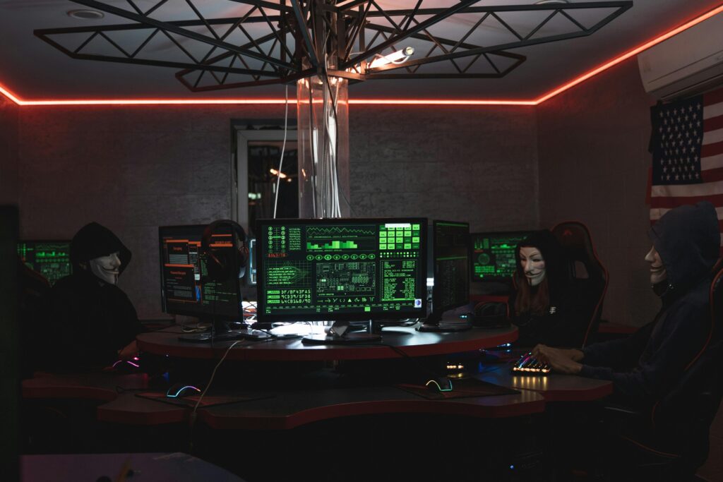 pexels-photo-5380649-5380649 Team of hackers with Guy Fawkes masks coding in a dark room with computers.